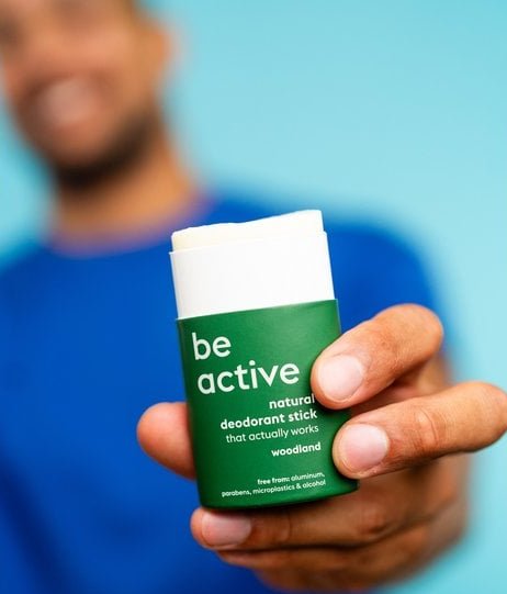 Mand i blå trøje holder en naturlig deodorant stick med grøn etikette, der siger "be active". (1)