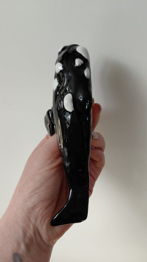 Hånd, der holder en sort og hvid keramisk figur formet som en spækhugger. (7)