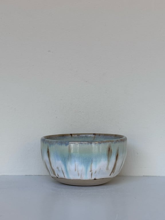 Lyseblå og hvide keramikskål med brunlige dekorative streger på en grå overflade foran en lys væg.