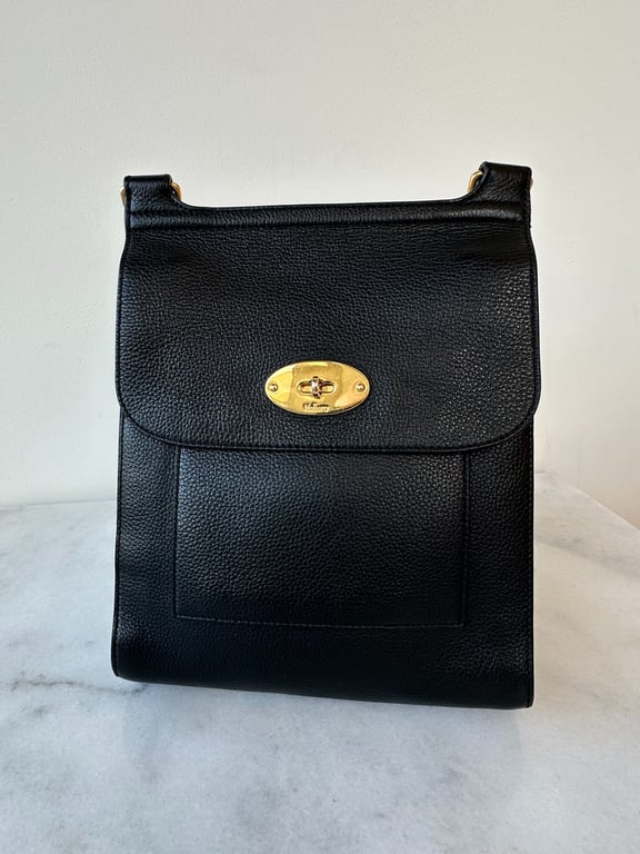 Sort lædertaske med gyldent drejelås foran, placeret på en marmoroverflade.