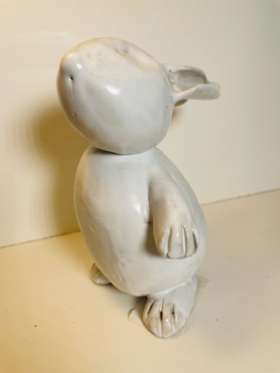 Hvid keramisk figur af en stiliseret pingvin med detaljerede fødder og vinger, stående på flad overflade.