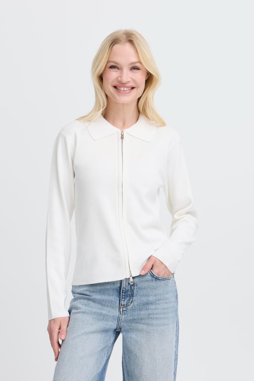 Kvinde iført hvid lynlåsjakke med krave og lyseblå jeans, smilende mod kameraet.