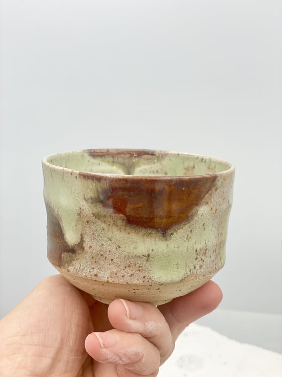 Hånd der holder en keramisk kop med grønne og brune glasurachle.