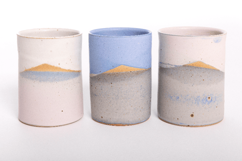 Tre keramiske krus med landskabsdesign, hver med en fjeld- og sølandskab i forskellige pastelfarver: hvid, blå og grå.