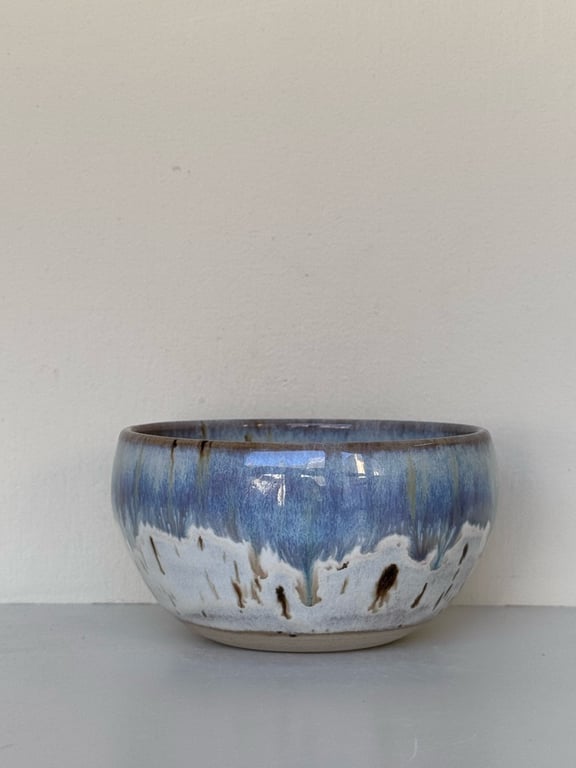 Keramisk skål med blå og hvid glasur, placeret på en grå overflade mod en lys væg.
