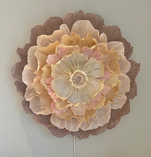 Stor blomst af papir med flere lag i beige, lyserøde og brune nuancer på en lys væg. (1)