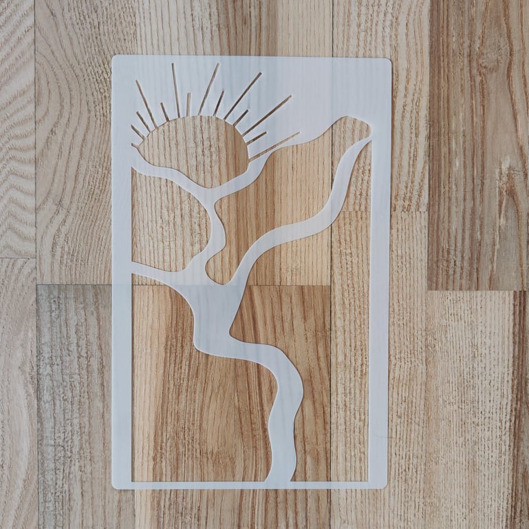 Hvid stencil med abstrakt motiv af sol, gren og fugl på træbord.