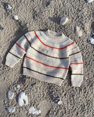 En strikket trøje med brede, vandrette striber i rødt og gråt, lagt på sand med muslingeskaller spredt omkring. (1)