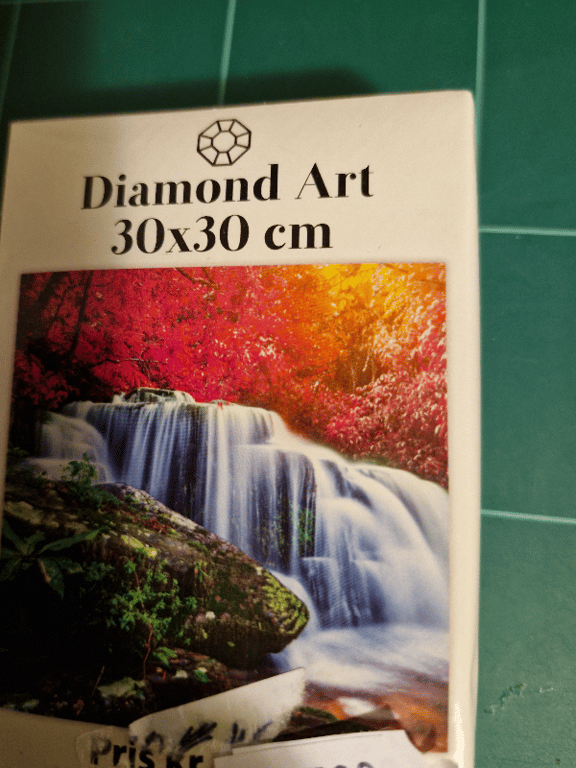 Billede af en Diamond Art pakke med et motiv af et vandfald omgivet af farverige træer i røde og orange nuancer, størrelse 30x30 cm.
