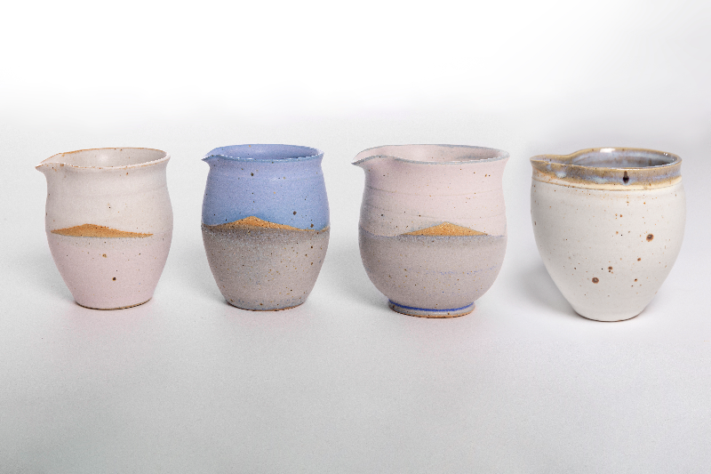 Fire keramiske krus i forskellige farver og teksturer, hver med en rustik, håndlavet stil. (6)