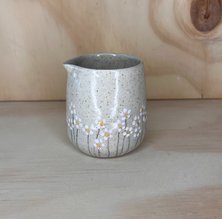 Keramisk lille kande med blomsterdekoration i hvide og beige nuancer på beige baggrund, placeret på lyst træ.