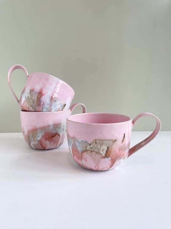 Tre rosa keramikkopper med kunstneriske, abstrakte mønstre i brun og grå, placeret mod en neutral baggrund.