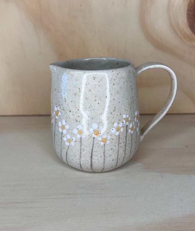 Keramisk kande med håndmalede hvide og gule blomster på beige baggrund.