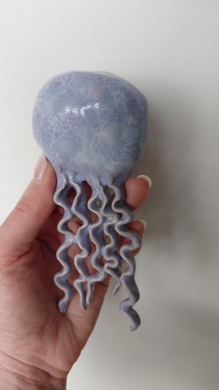 Hånd, der holder en lilla og blå keramikfigur formet som en meduse med krøllede tentakler.