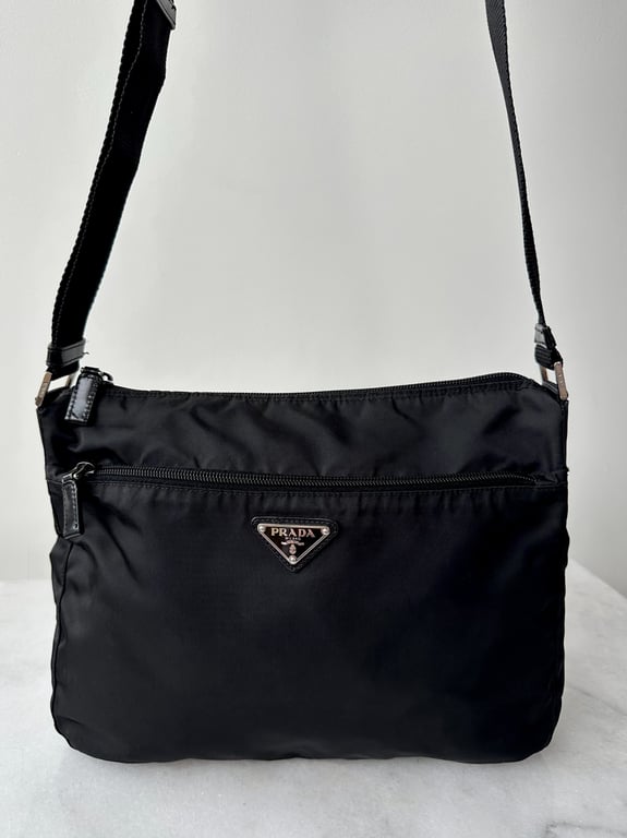 Sort Prada skuldertaske i nylon med justerbar rem og lynlåslomme foran.