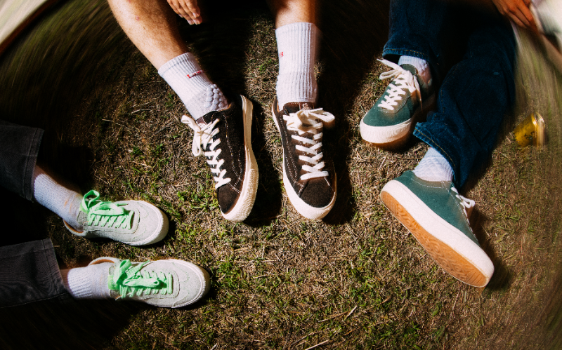 Fire personer sidder på græsset med forskellige sneakers og hvide sokker på.