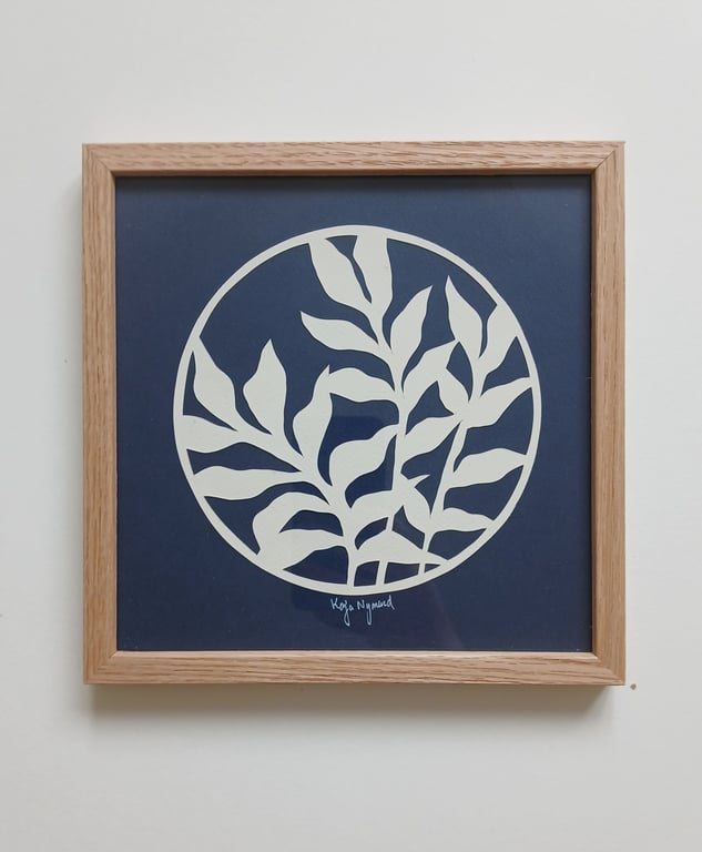 Billede af en firkantet träramme med et bladmønster i hvidt på en mørkeblå baggrund, indrammet i en cirkel.