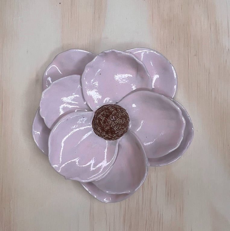 Glaseret keramik i form af en lyserød blomst med fem blomsterblade og en brun midte, lagt på en lys træflade.