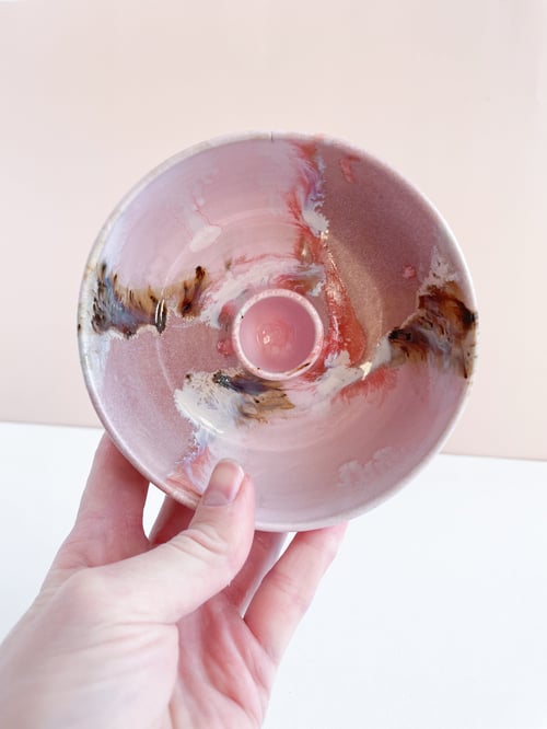Hånd, der holder en keramisk lysestage med pink, hvide og brune abstrakte farvemønstre. (1)