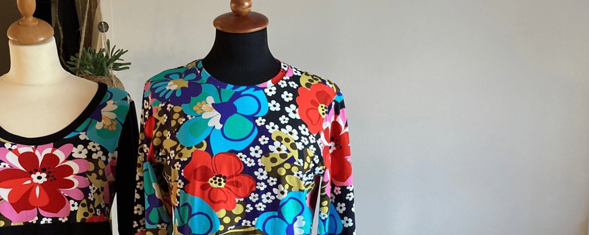 To mannequinbustes iført farverige kjoler med store blomsterprint stående mod en ensfarvet væg.