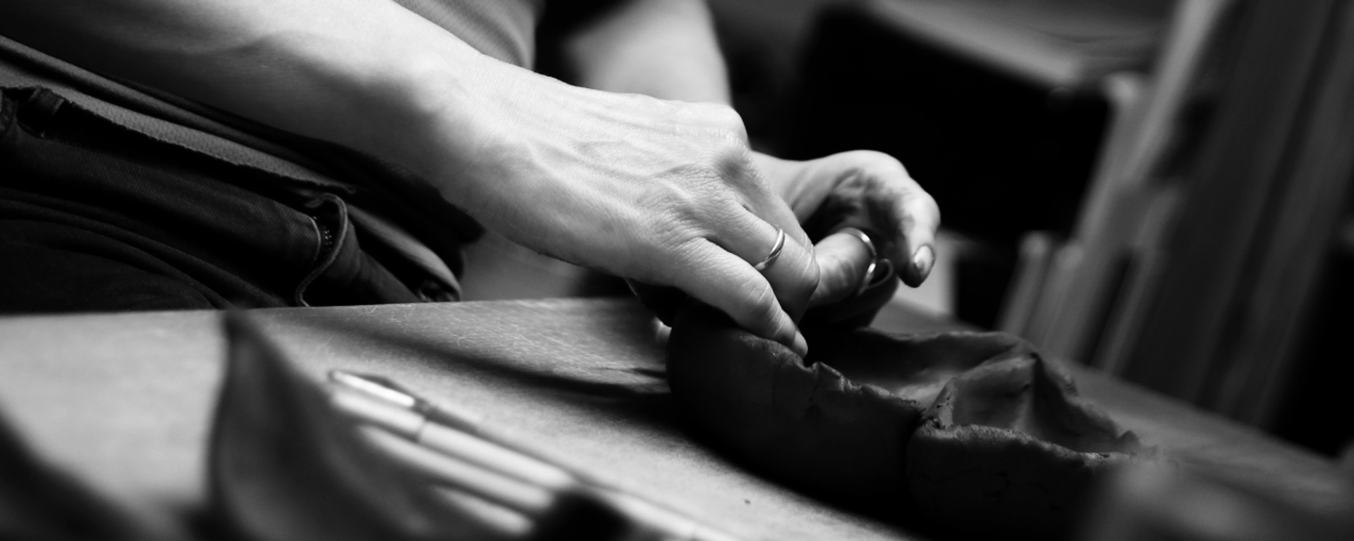Sort-hvid billede af hænder, der former ler på et bord, med en kniv liggende ved siden af.