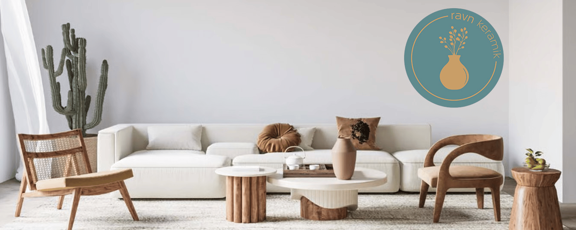 Stue med hvid sofa, to brune stole i træ og møbelstof, to runde sofaborde med vaser og dekorative genstande, stor kaktus i baggrunden og logo med teksten "ravn keramik" på væggen.