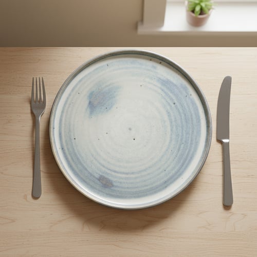 Tallerken med blå og hvide nuancer placeret på et lyst træbord, med en gaffel til venstre og en kniv til højre.