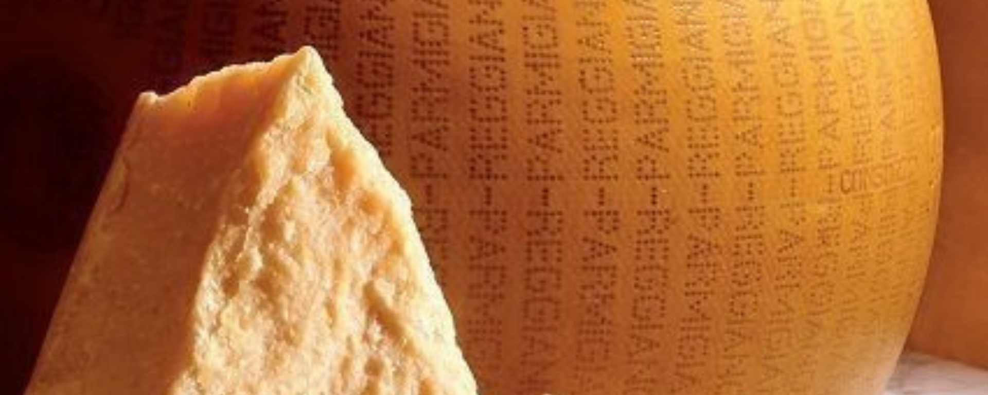 Et close-up af et stykke parmesanost med en rund ost i baggrunden og teksten "Få en gratis, økologisk tomatplante med, når du afhenter på vores lager" i nederste højre hjørne.