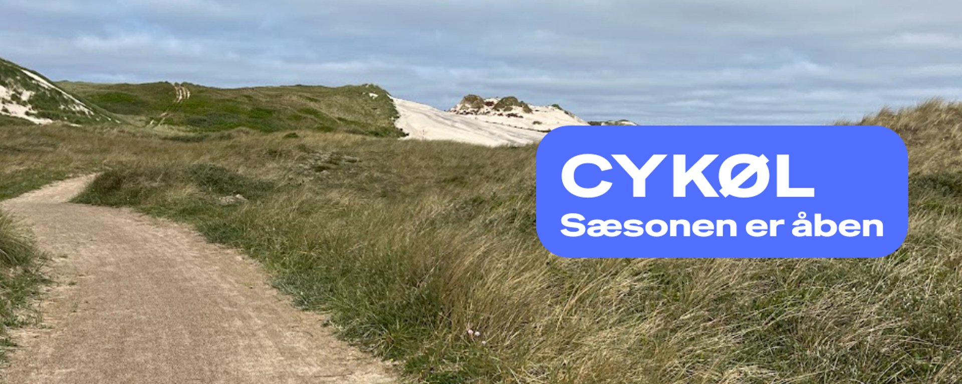 Sti gennem klitlandskab med græs og sandklitter under en overskyet himmel, overlejret med blå tekstboks med teksten "CYKØL Sæsonen er åben".
