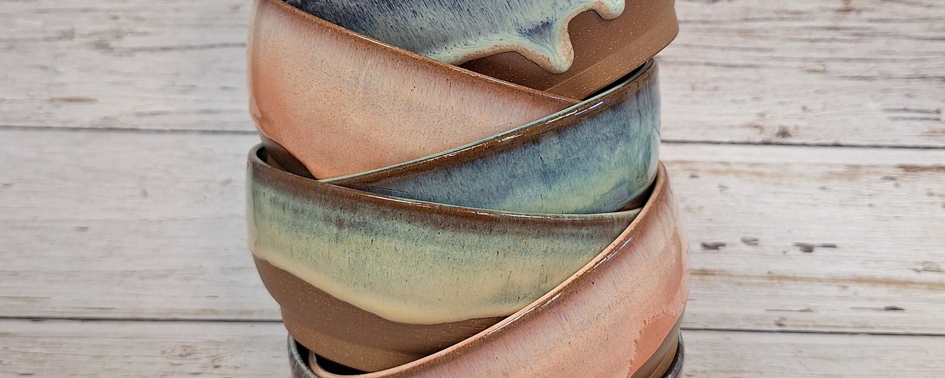 Stablet sæt af seks keramiske skåle med glasur i blå, grønne og rosa nuancer på træbord.