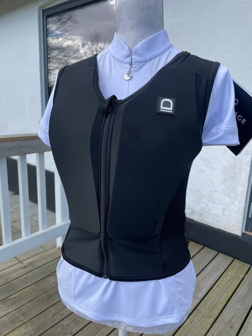 Sort ridevest med lynlås foran på hvid mannequin iført hvid skjorte, stående på træterrasse udenfor. (1)