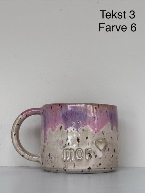 Keramikkrus med lilla og beige glasur, indgraveret med teksten "mor" og et hjerte, stående på en grå overflade. (1)