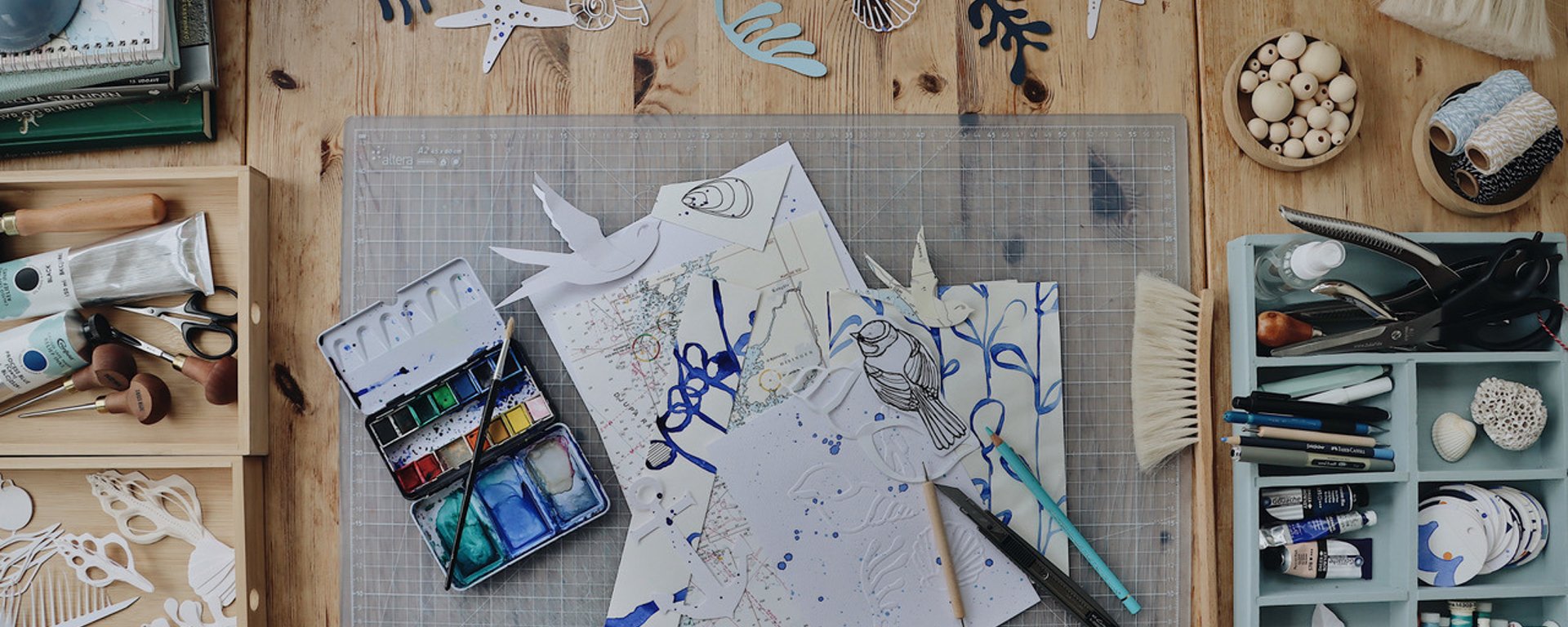 Tegnet sort-hvidt billede af et keramikværksted med drejeskive, bord med ler og keramikværktøj, hylder med ler og færdige krukker samt en ovn til brænding af keramik.