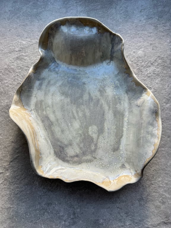 Uregelmæssigt formet keramisk skål med grå og beige glasur, placeret på en stenoverflade.