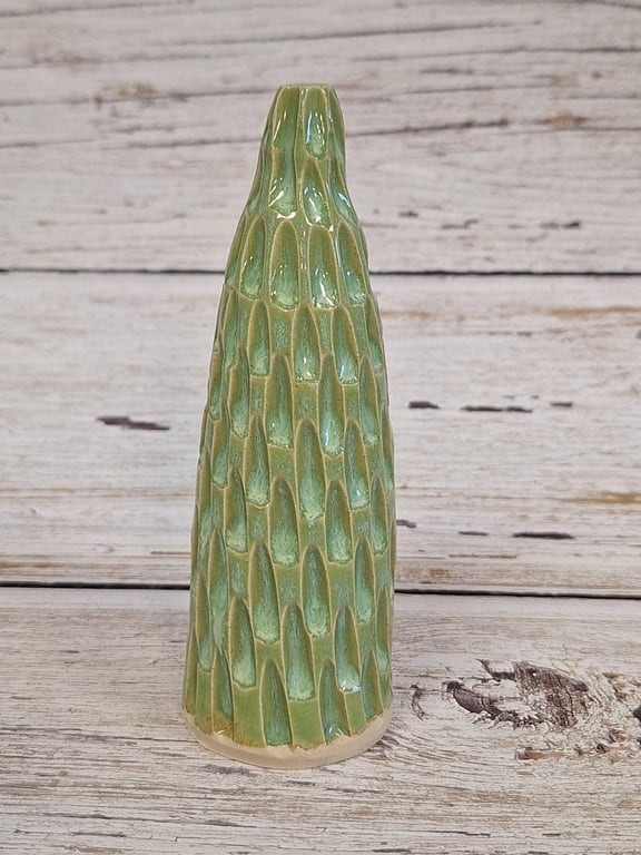 Grøn keramisk vase med riflet overflade stående på lyst, rustikt træbord.