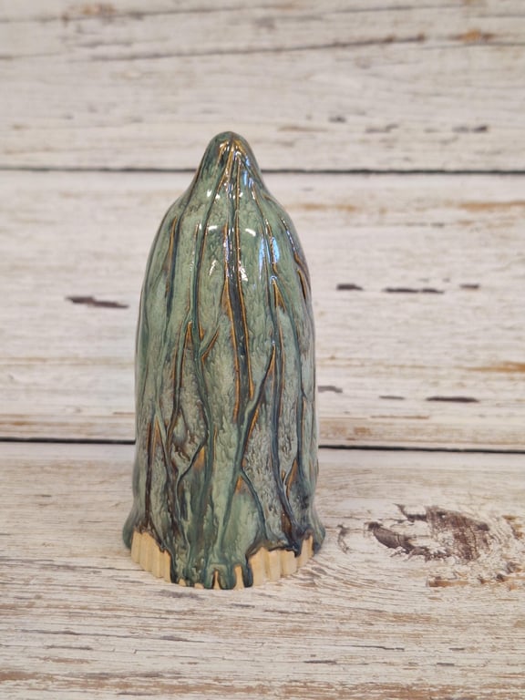Grøn og brunt glasur-dækket keramisk figur formet som et kegle med teksturerede linjer, placeret på et lyst træbord.