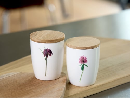 To hvide keramikbeholdere med blomsterdekoration og låg af træ, placeret på et lyst træbord. (1)