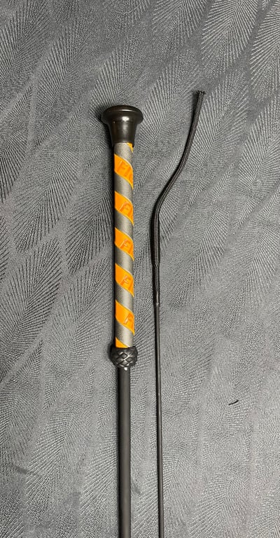 To sorte ridespor med orange og grå detaljer, lagt på et mønstret gråt tæppe.