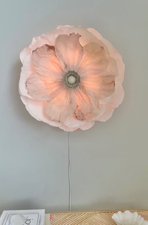 Væglampe formet som en stor, lys rosa blomst med bløde, lagdelte kronblade, der giver et varmt skær.