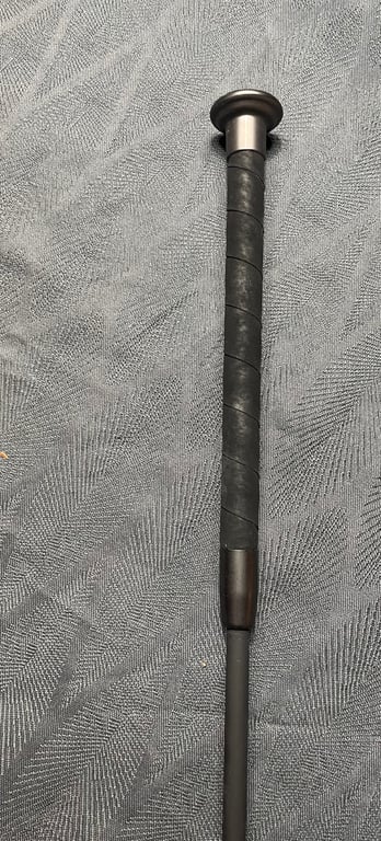 Sort baseballbat med sort greb liggende på grå tæppe.