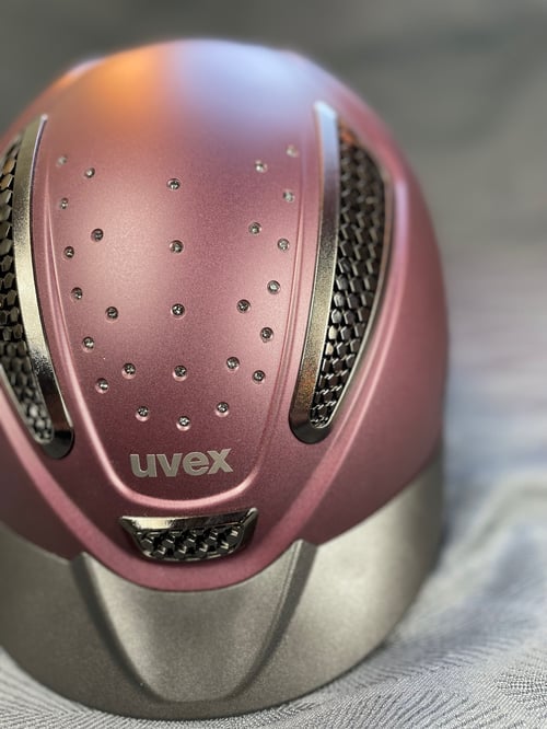 Lyserød og sølv cykelhjelm med ventilationsåbninger og små dekorative nitter, mærket "uvex". (1)