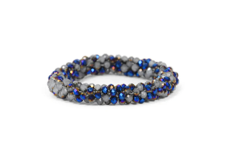 Armbånd lavet af snoede, glinsende perler i blå, grå og guld farver på hvid baggrund.
