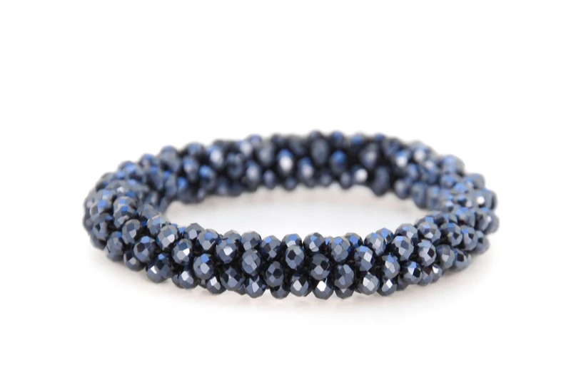 Blåt armbånd lavet af facetterede perler samlet i en snoet cirkulær form på hvid baggrund.