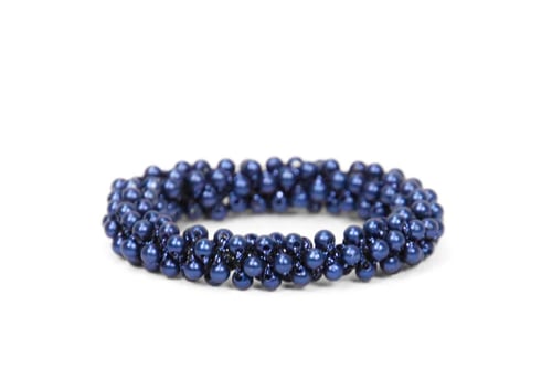 Mørkeblå armbånd lavet af glinsende perler samlet i et flettet mønster mod en hvid baggrund. (1)