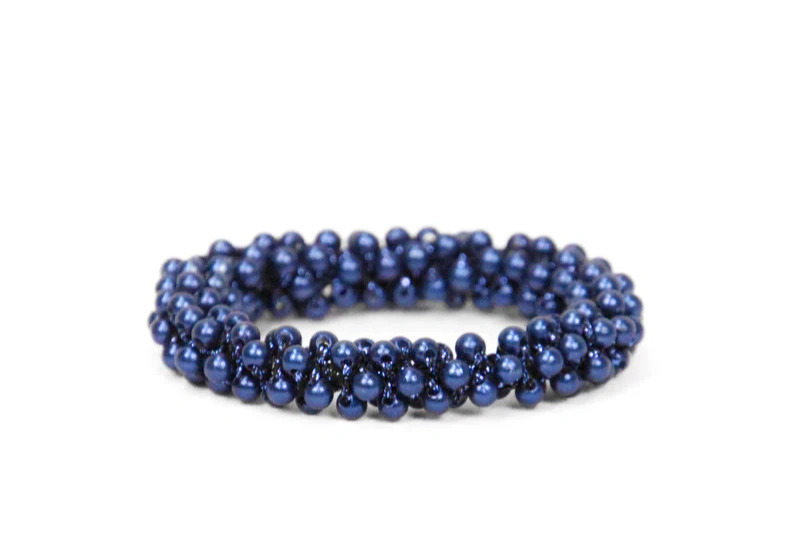 Mørkeblå armbånd lavet af glinsende perler samlet i et flettet mønster mod en hvid baggrund.