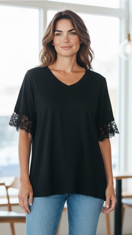 Kvinde iført sort T-shirt med blonder på ærmerne og blå jeans, stående indendørs foran vindue.