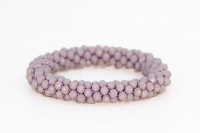 Lavendelfarvet armbånd lavet af små, facetterede perler trukket sammen i et flettet mønster.