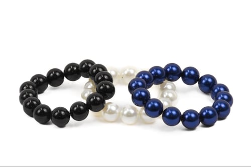 Tre elastiske armbånd med perler i farverne sort, perlemor hvid og mørkeblå, arrangeret på hvid baggrund. (1)