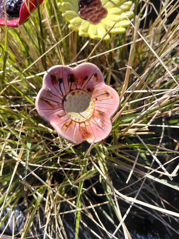 Keramisk pink blomstdekoration placeret i tør græs.