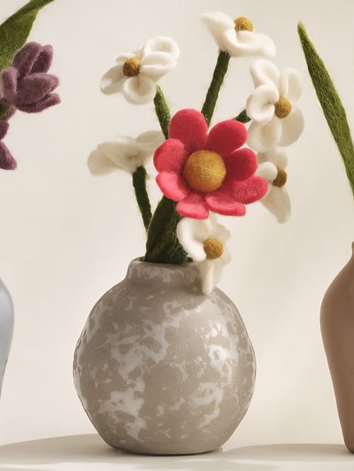 En rund gråblomstret vase med filtblomster i lyserød, hvid og grøn. (1)